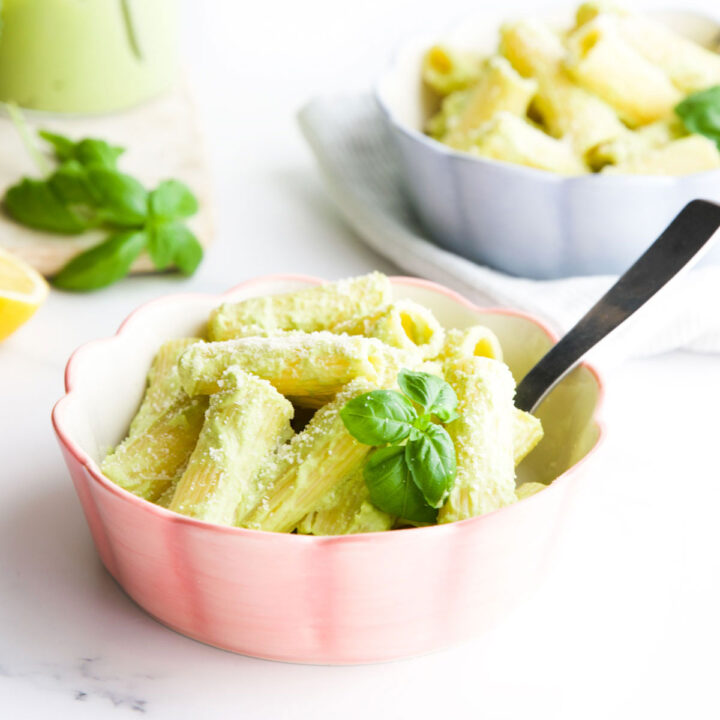 Broccoli Pesto Pasta in Two Bowls With Basil and Sauce in Background.