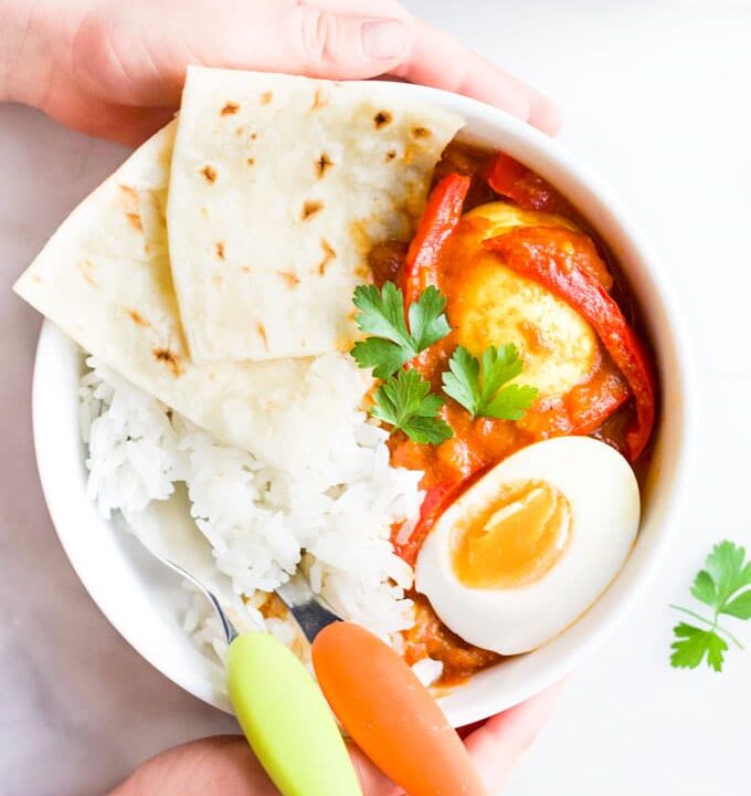 Child Holding Bowl of Egg Curry with Rice and Roti Bread
